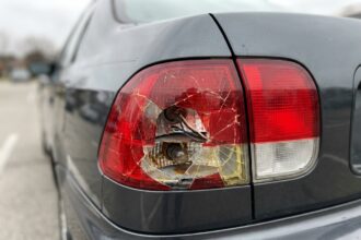 Feu arrière de voiture endommagé avec plastique fissuré et oxydation visible sur un parking